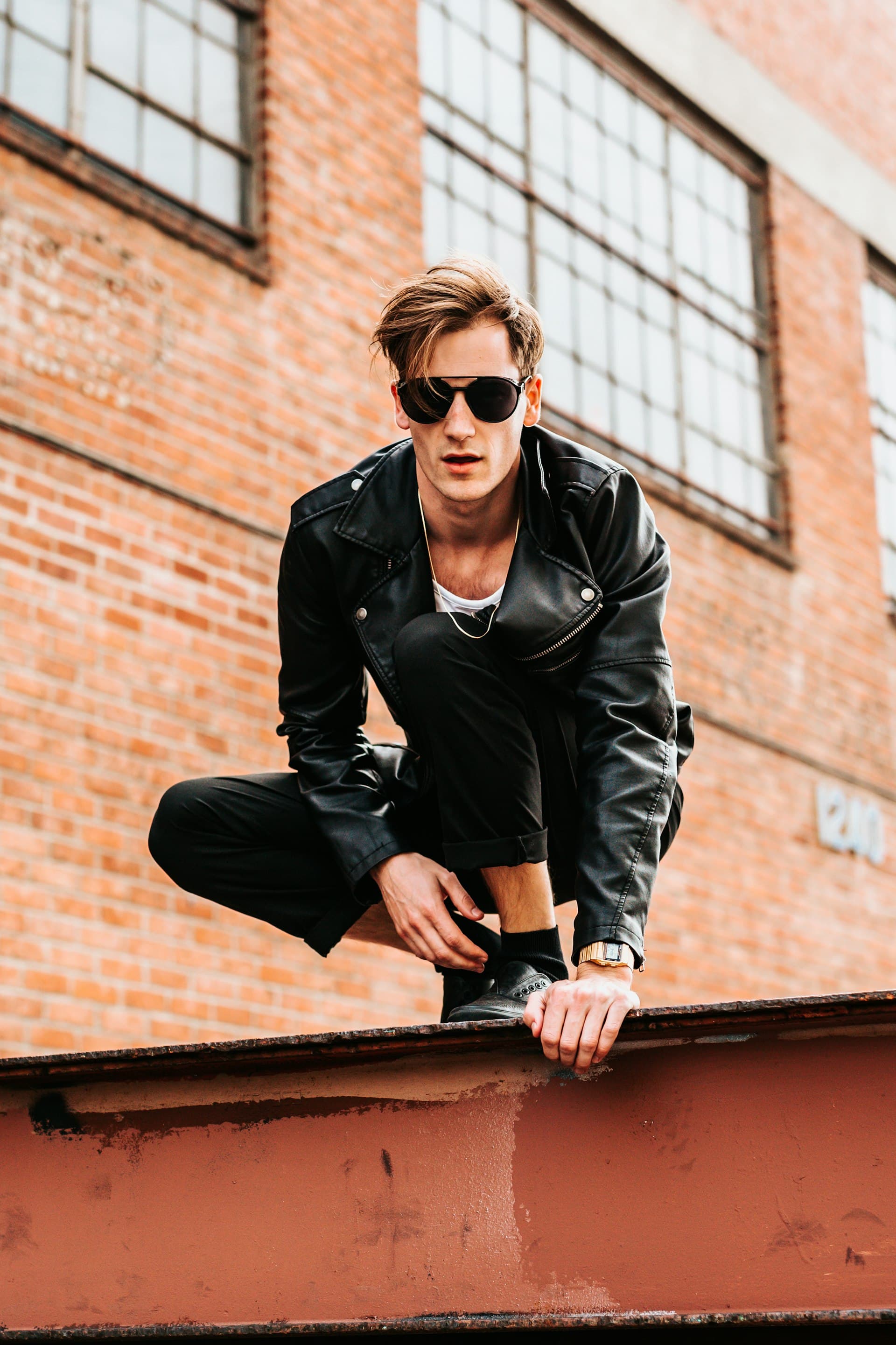 Man in a black leather jacket against a brick facade